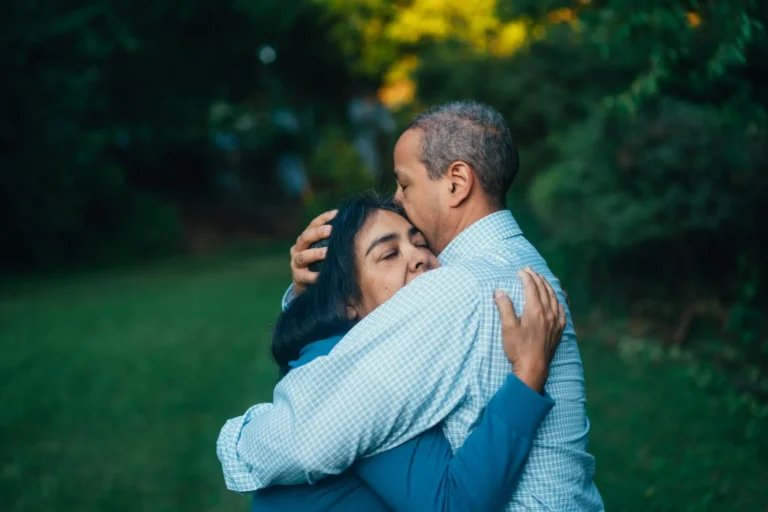 Man holding his partner in a long hug under the trees