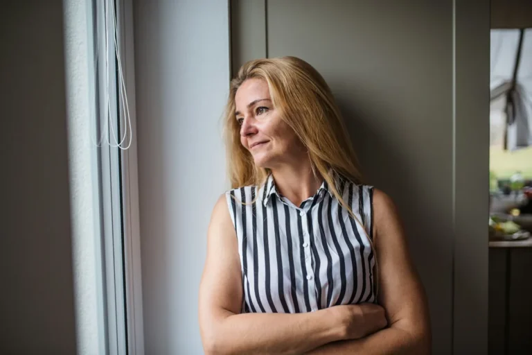 Woman in her fifties standing by a window, looking out
