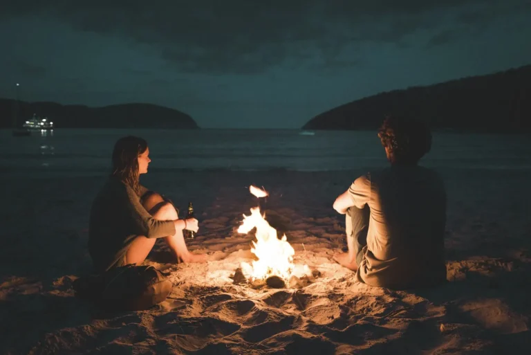 Couple sitting by a fire on the beach at dusk