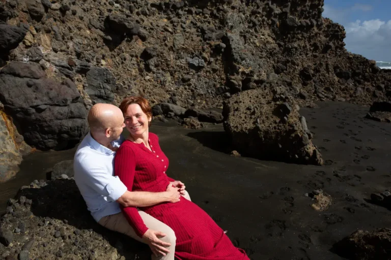 Tarisha resting back against Mark on the rocks at Piha