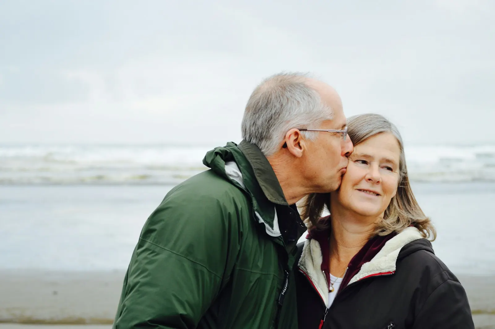 Man kissing his partner on the cheek by the sea