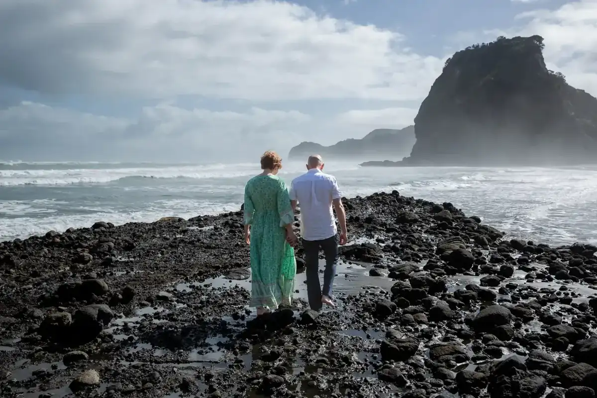 Tarisha and Mark walking hand in hand towards Lion Rock at Piha