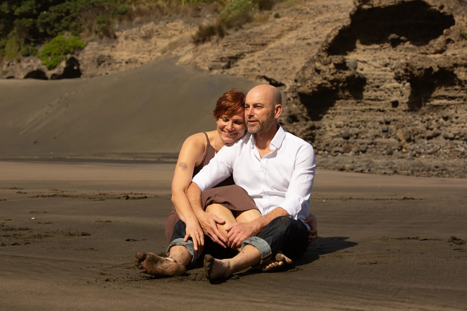 Tarisha and Mark sitting together on the sand at Piha, Auckland