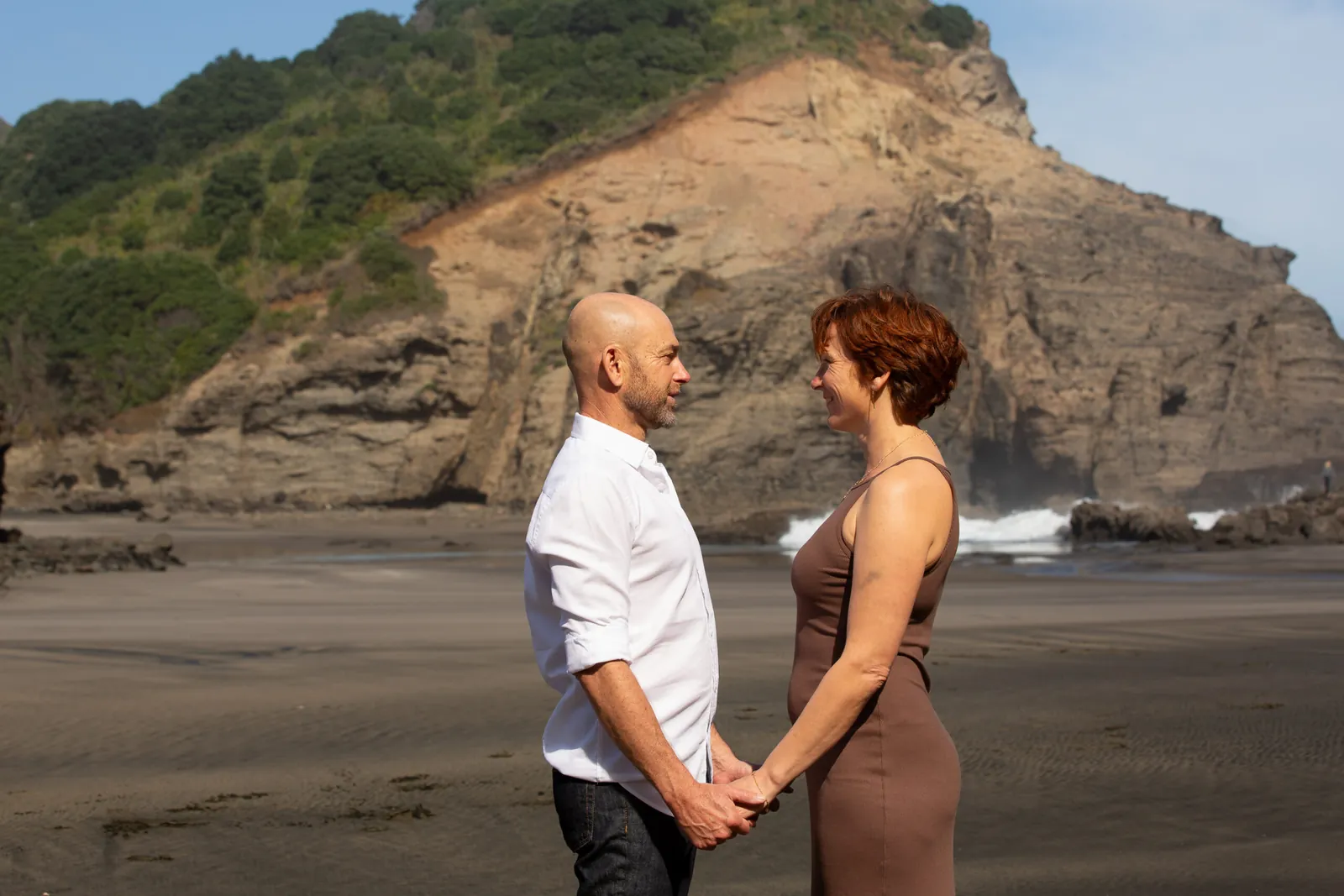 Tarisha and Mark standing face to face holding hands on Piha beach